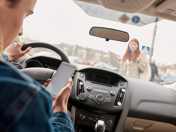 Driver looking at phone while driving with a pedestrian in the walkway